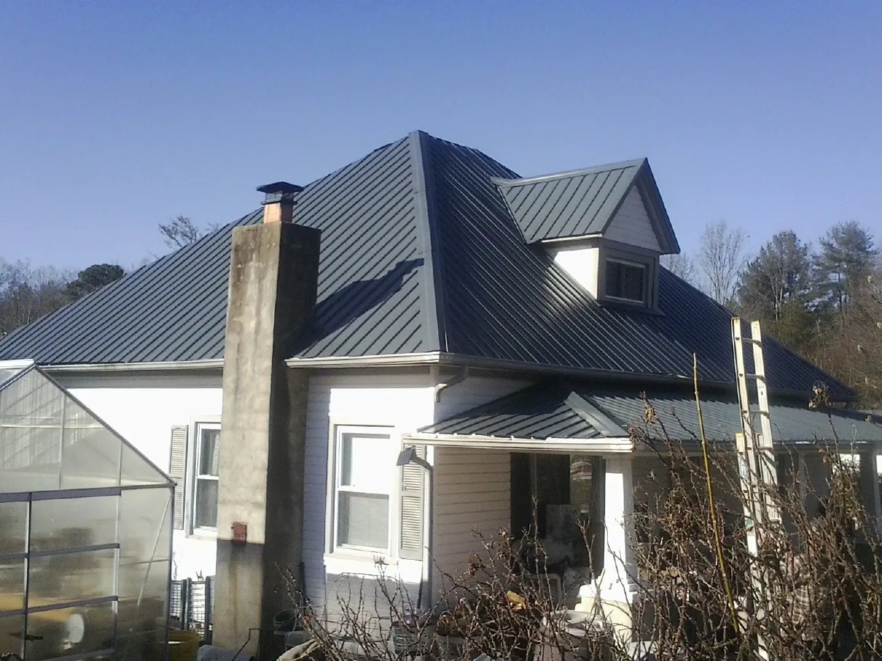 Dark blue standing seam metal roof on a white farmhouse with dormer — Slate & Tile Roof Repair by Roofing Brothers in Nalcrest