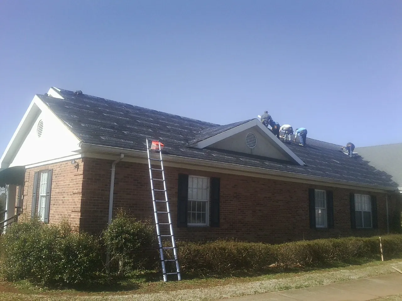 Crew tearing shingles off a brick ranch roof with a ladder set — Metal Roof Repair work by our crew in Nalcrest
