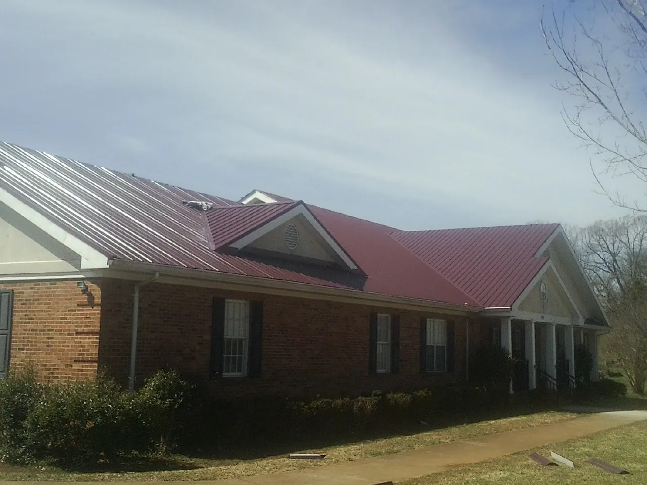 Red metal roof with gabled entries on a long brick building, from a Hail Damage Roof Repair job in Nalcrest