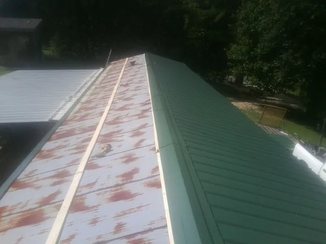 Old rusted panels beside newly installed green metal roofing — Wind Damage Roof Repair by Roofing Brothers in Nalcrest