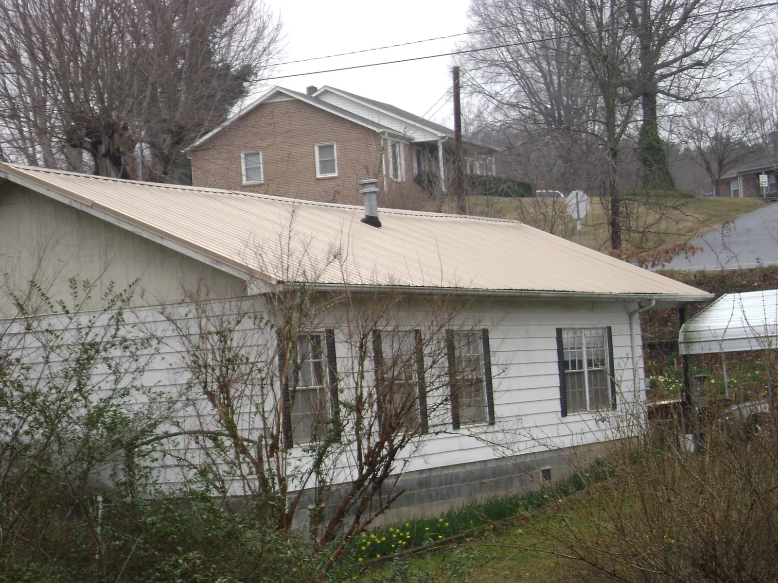 Tan metal roof on a white sided house set into a hillside — Commercial Roofing by Roofing Brothers in Nalcrest