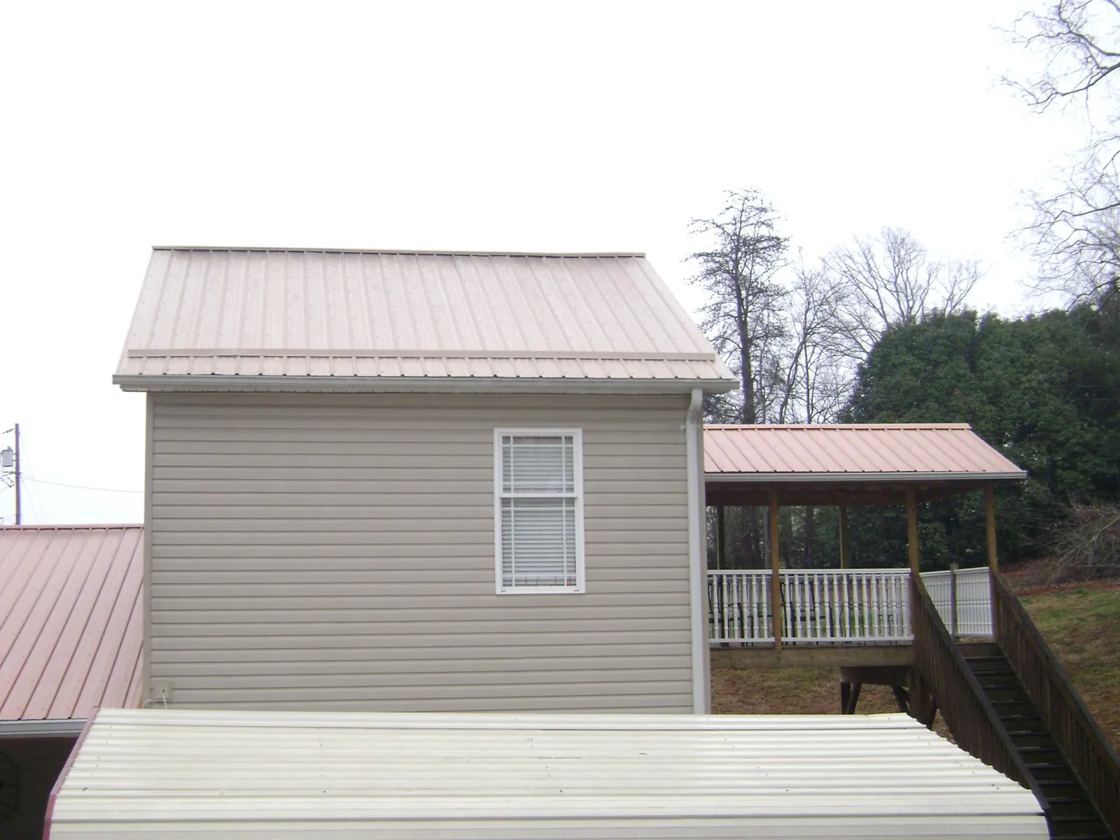 Tan metal roofs on a two story addition and attached porch, from a Roof Replacement job in Nalcrest